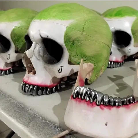 A row of stylized skulls with green tops and metallic teeth are displayed on a shelf.
