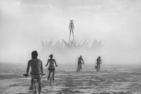 Cyclists approach the Man at Burning Man festival through a dusty haze.