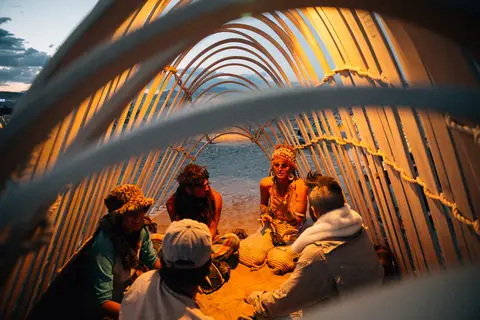 A group of friends gathers inside a geodesic dome structure at dusk, illuminated by warm interior lights.
