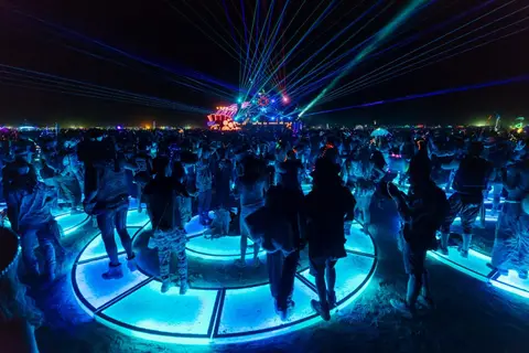 A crowd dances under a dazzling laser light show at a nighttime festival.