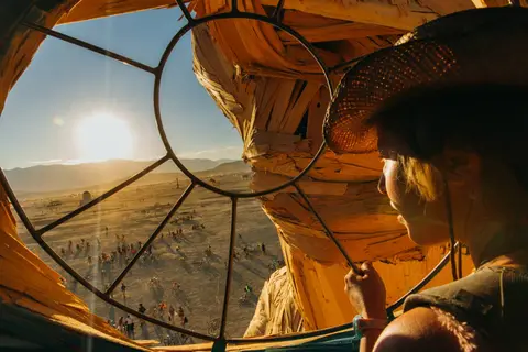 A person in a straw hat looks out from a unique structure at a desert landscape during sunset.