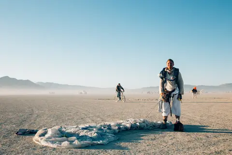 A person stands in a vast, dusty desert landscape with mountains in the distance under a clear blue sky.