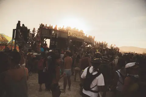 A large crowd gathers at a dusty outdoor festival stage during golden hour.