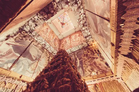 An upward shot captures the intricate, mural-covered ceiling of a structure, with a textured, conical object dominating the foreground.