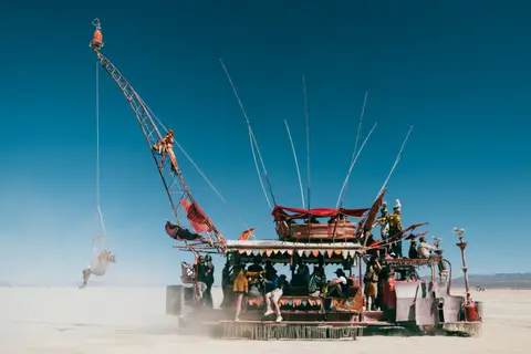A large, elaborate art car resembling a ship is driven across the playa at Burning Man.