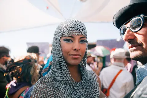 A woman in chainmail and a man in a top hat pose for a photo at an outdoor event.