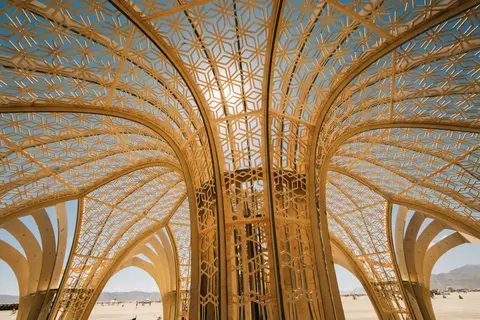 Intricate golden latticework forms a canopy over a desert landscape under a bright blue sky.