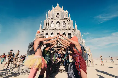 A group of people form a human archway in front of a large, ornate temple structure on a sunny day.