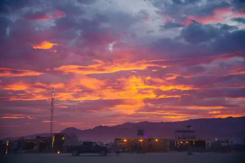 Vibrant orange and purple clouds streak across the sky above a silhouetted desert landscape at dusk.