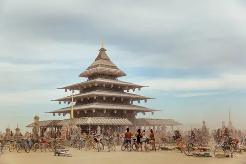 A multi-tiered pagoda-like structure stands tall amidst a dusty landscape dotted with bicycles and people.