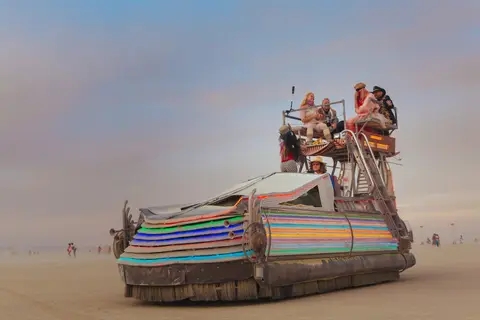 A colorful, art car shaped like a shoe cruises across the dusty playa at Burning Man.