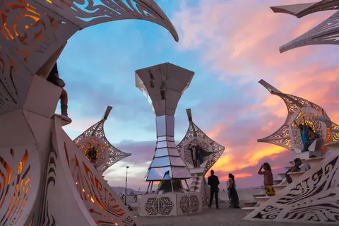 Intricate art installations glow under a vibrant sunset sky at Burning Man.